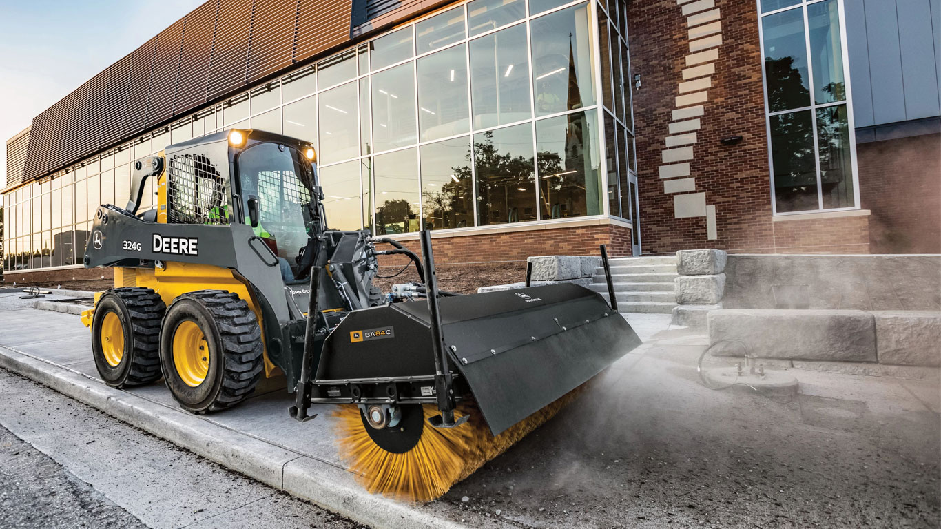 John Deere Skid Steer with Angle Broom attachment sweeping sidewalks in front of business.